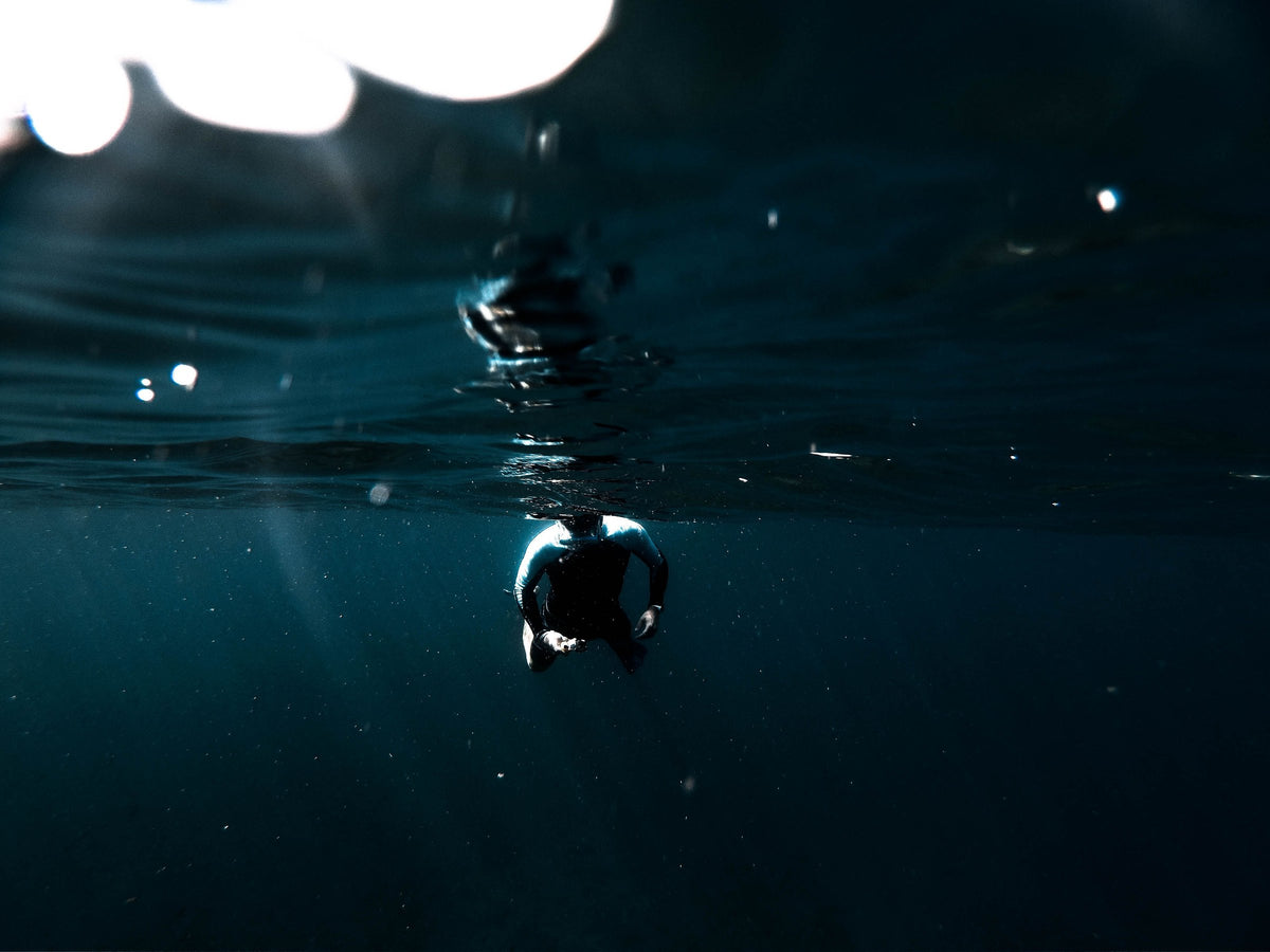 A lone diver silhouetted at a dark water surface with deep water below