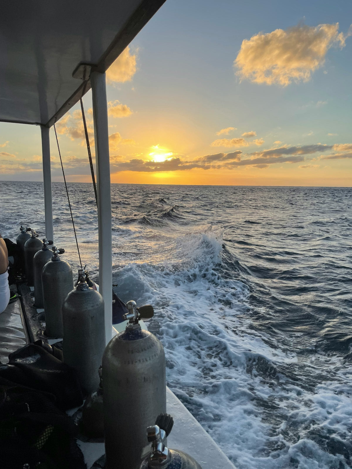 Row of scuba cylinders racked along a dive boat rail at sunset, wake and open sea beside, Cozumel, Mexico