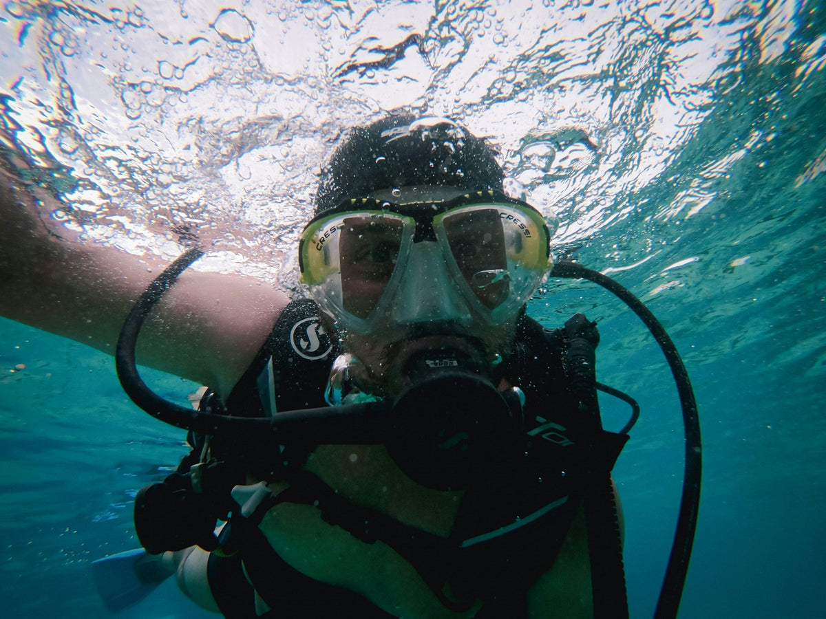 Close-up of a diver just under the surface breathing from a regulator, sunlit ripples above