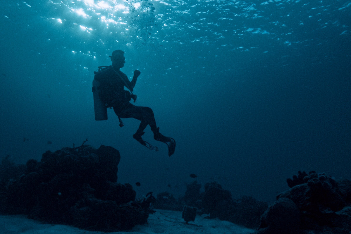 A single scuba diver in mid-water with the sunlit surface far above