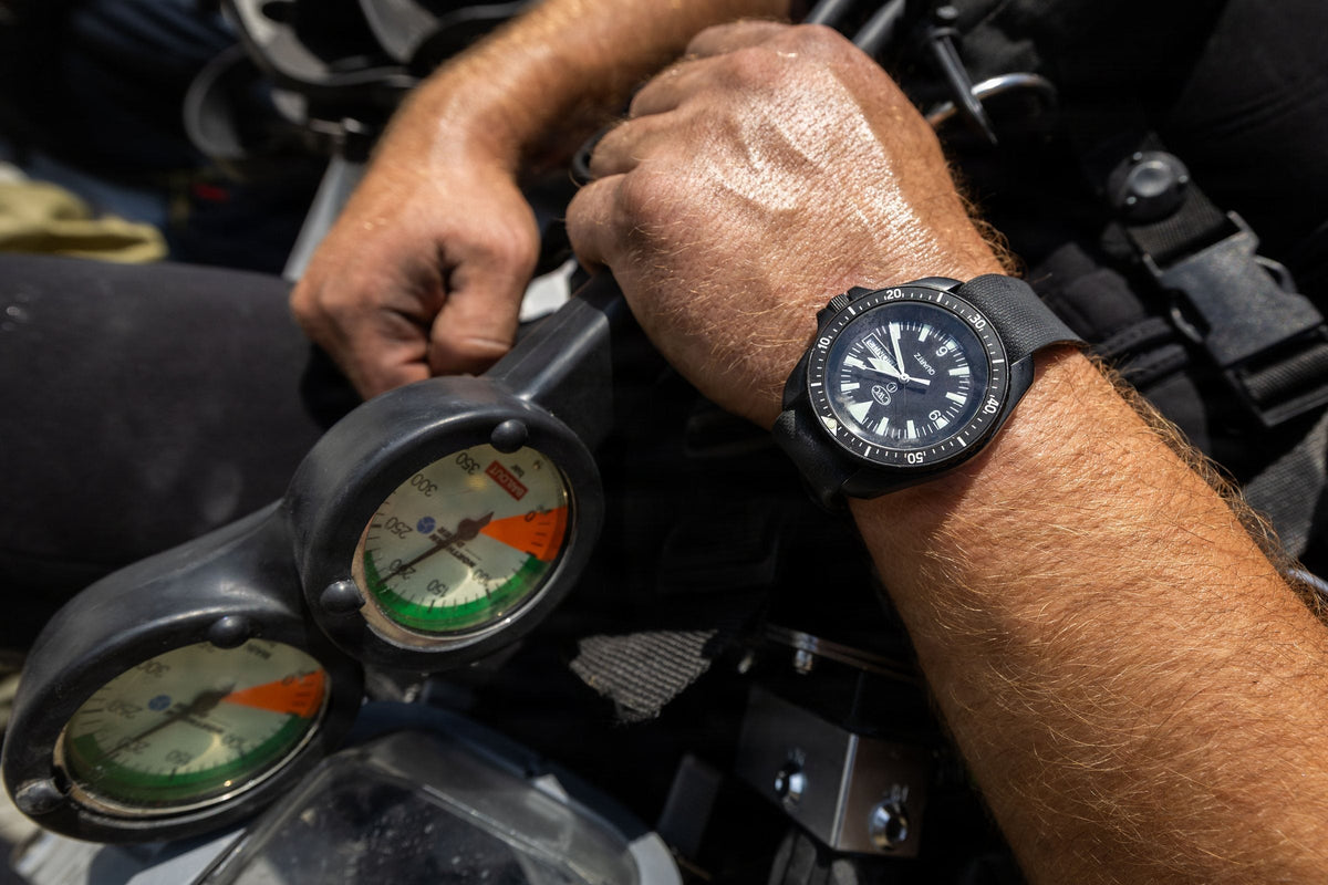 Close-up of a diver's hands on a twin analogue pressure gauge console, dive watch on the wrist