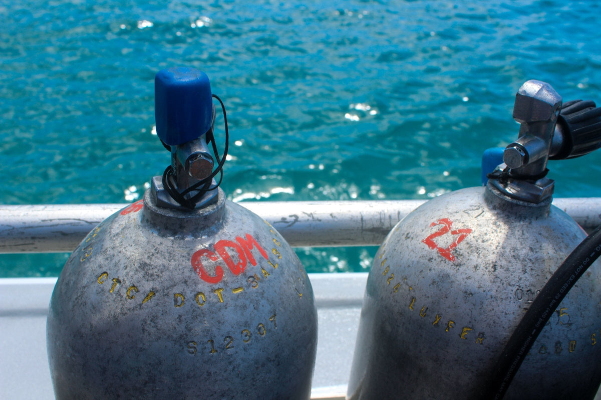 Two scuba cylinders standing on a boat deck, neck stamps and painted markings visible.