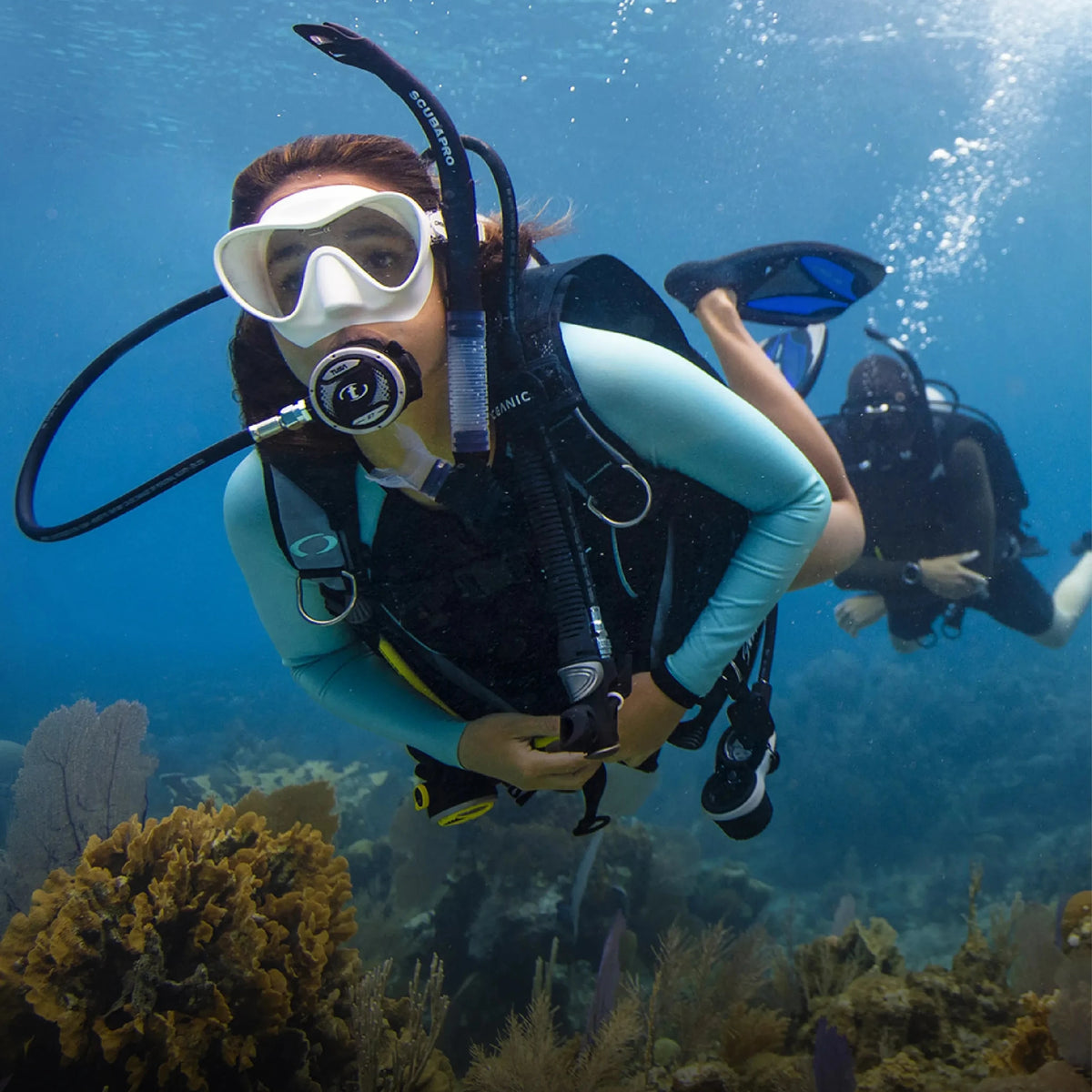 A diver swimming over a reef with a buddy behind