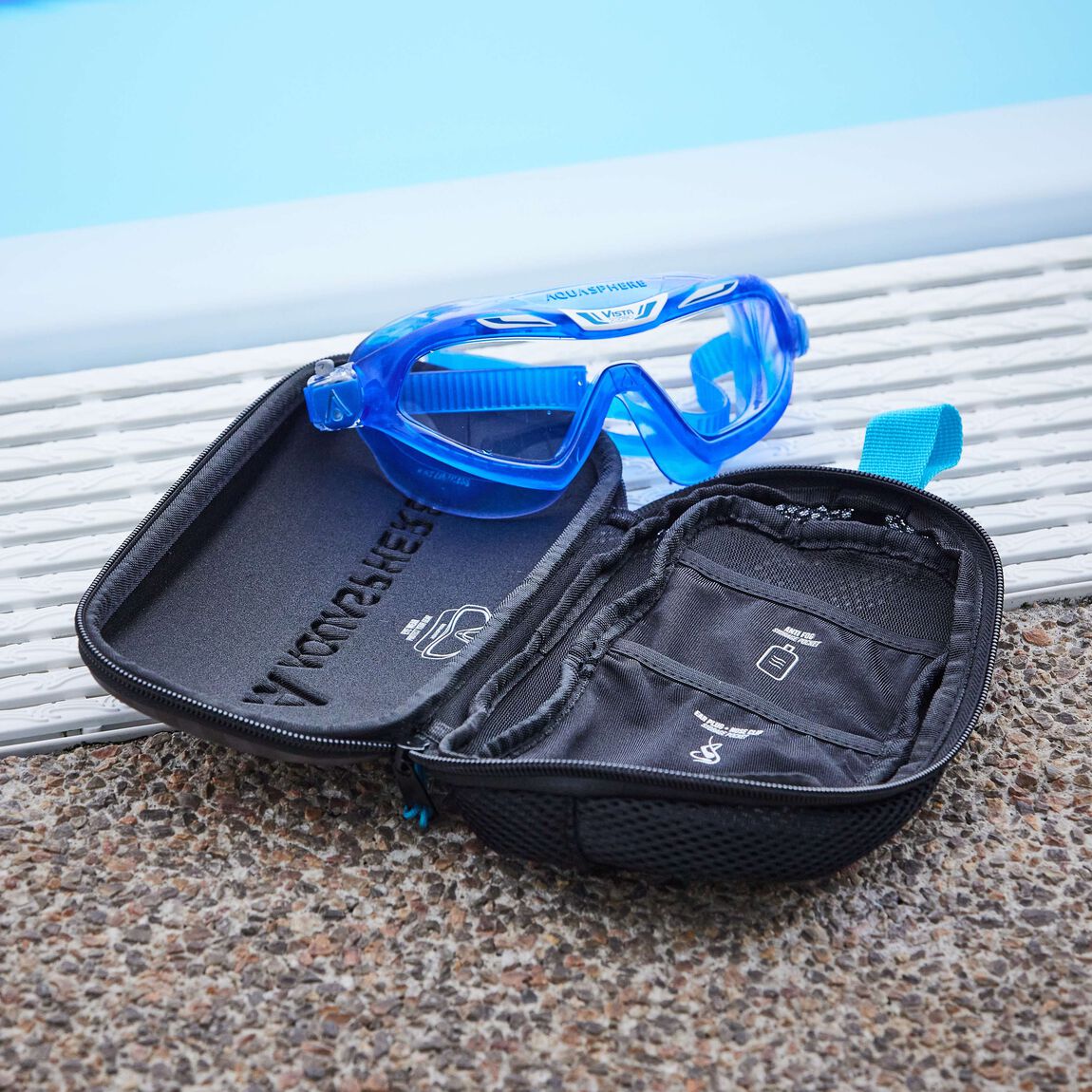 Blue swim mask placed on the open mask case beside a swimming pool
