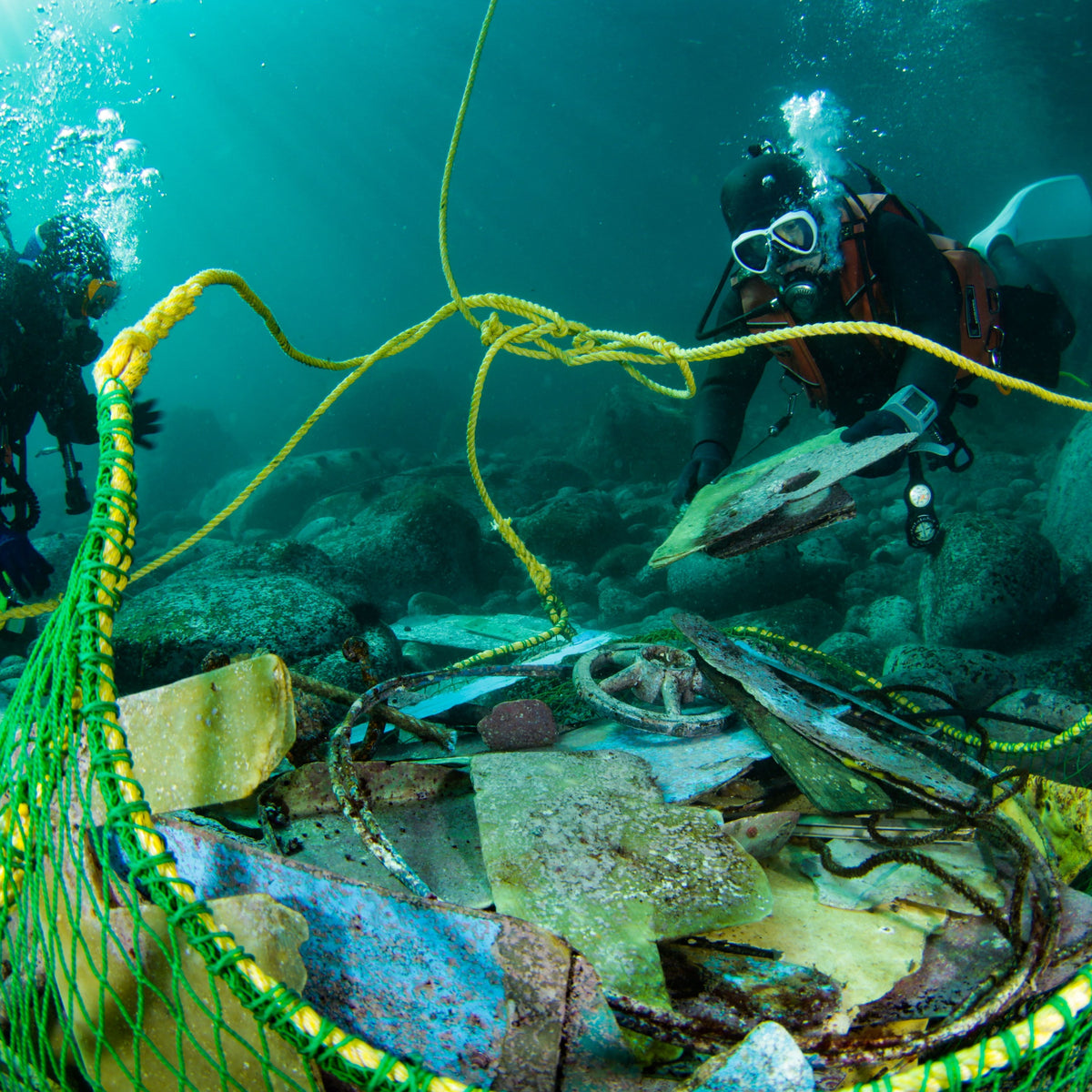 Divers filling a mesh bag with rubbish collected from the seabed