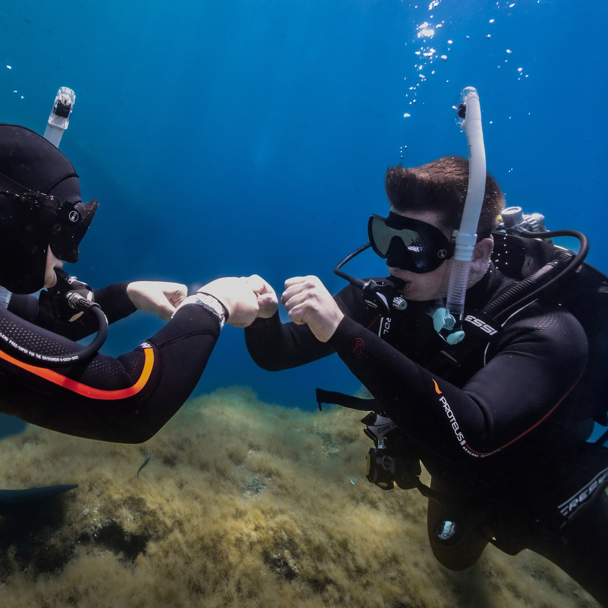 Two divers hovering in blue water and fist-bumping after a buoyancy skill