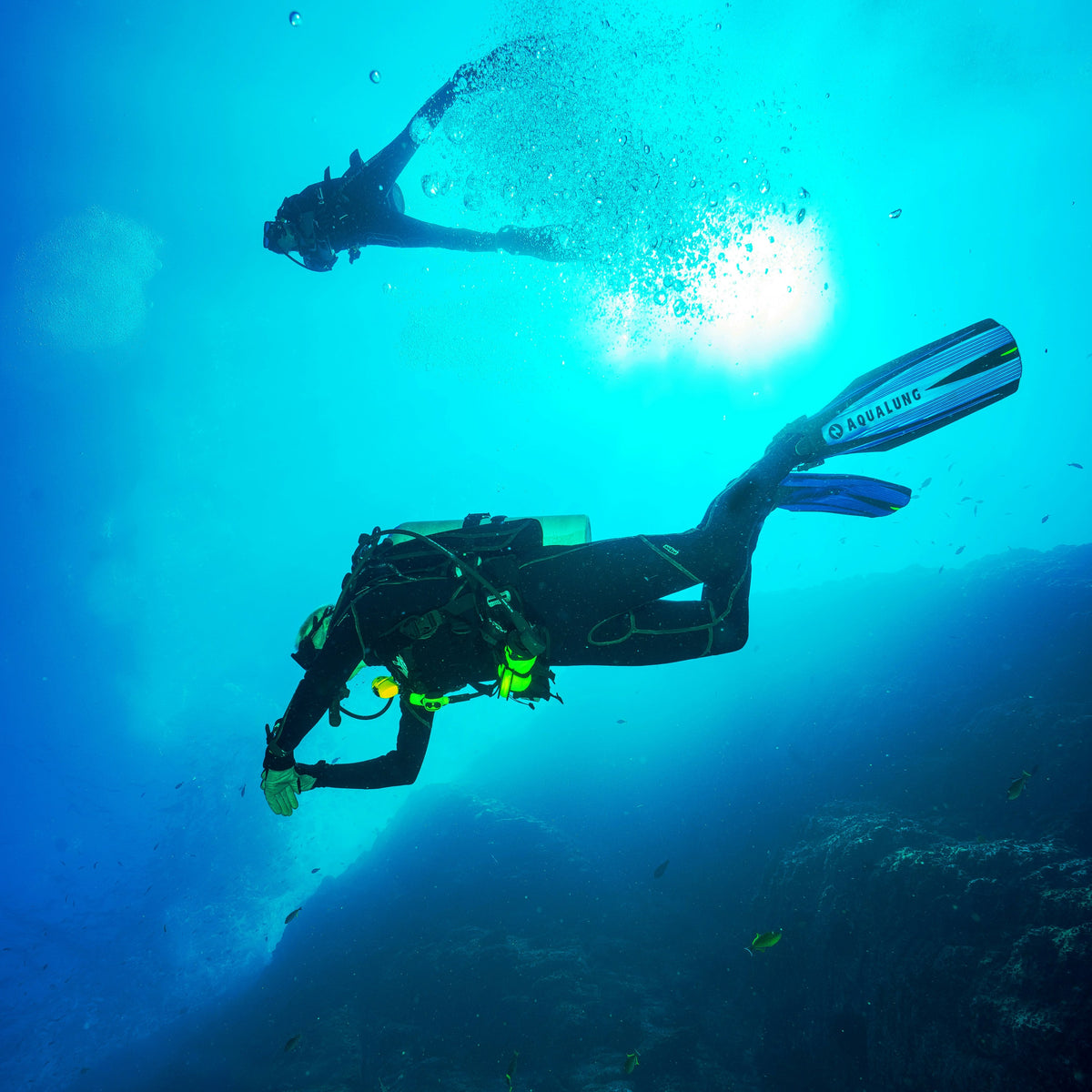 Diver in trim along a deep blue wall with a buddy descending above