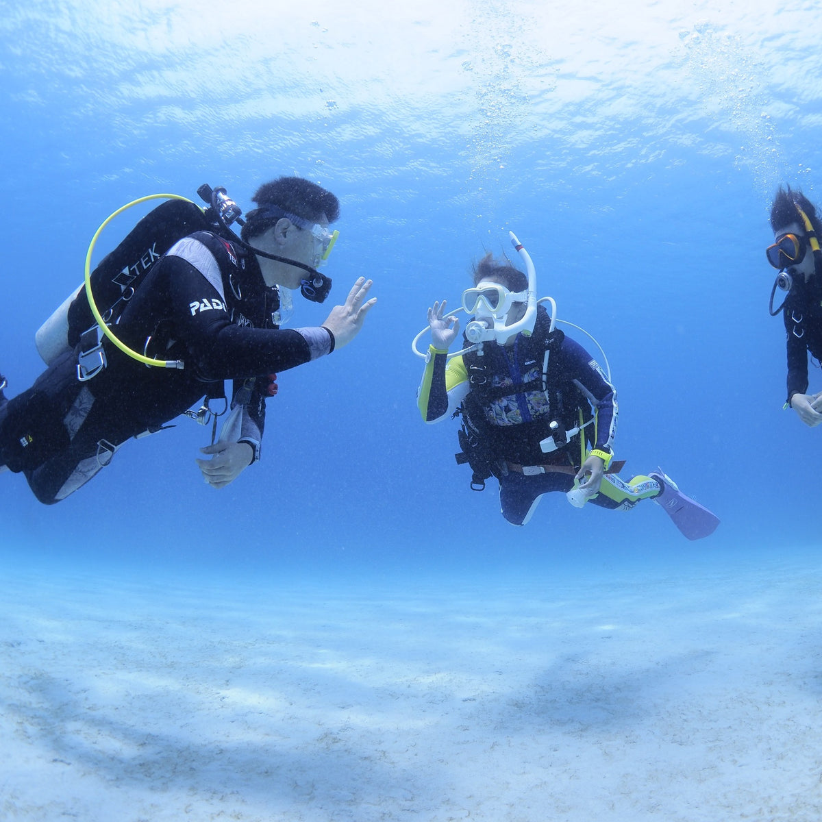 PADI instructor signalling to a student over white sand on a Scuba Diver dive