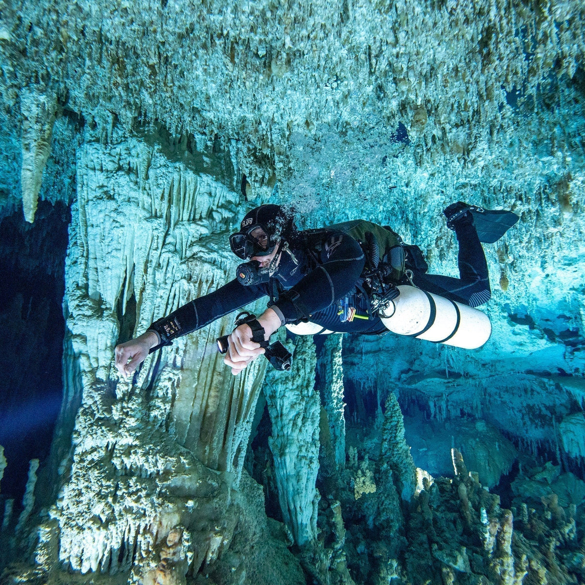 Sidemount diver with cylinders under both arms gliding through a decorated cave