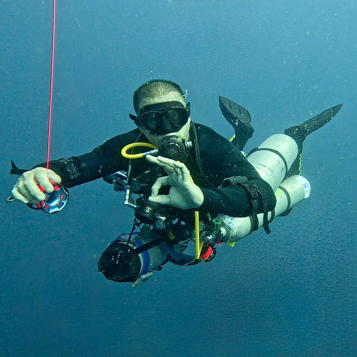 Sidemount technical diver with stage cylinders holding a line on a decompression stop