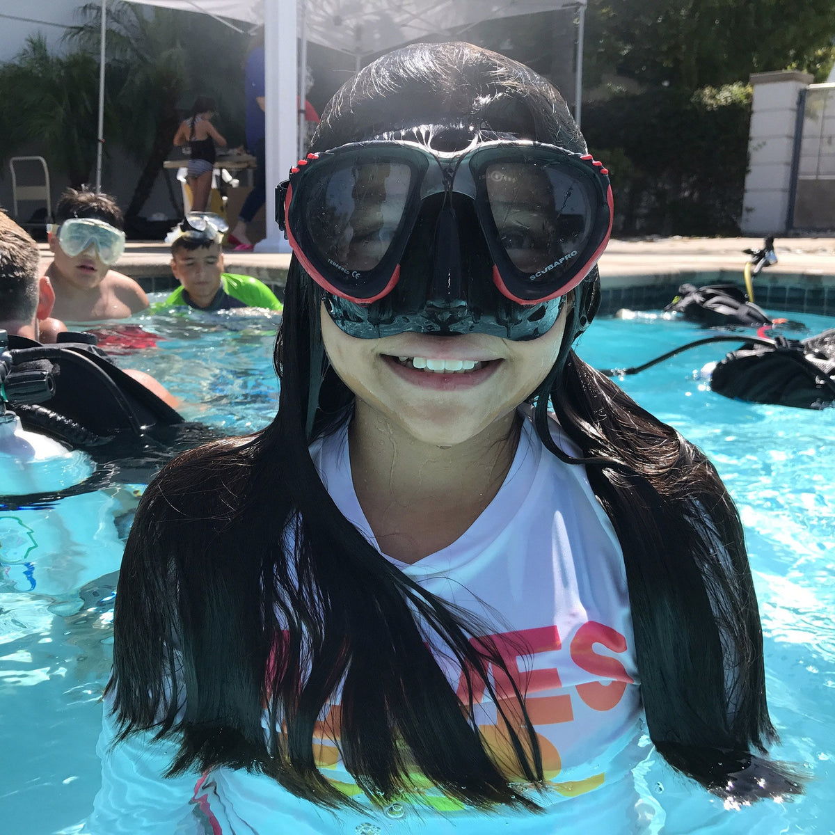 Child in a dive mask smiling at the pool edge on a PADI Bubblemaker session