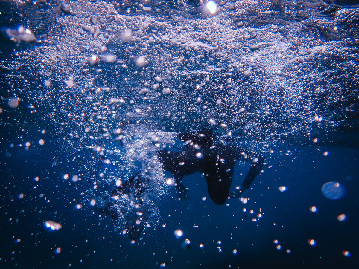 A diver silhouetted in a cloud of bubbles just below the surface on descent.