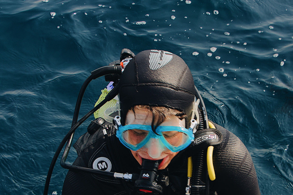 A diver at the surface at the end of a dive, hood on, head down and eyes closed.