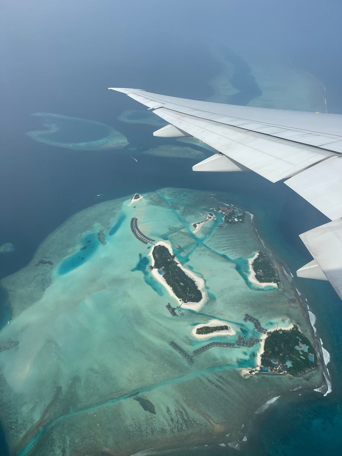 View from an airliner window: wing over a Maldives atoll with reef lagoons and resort islands