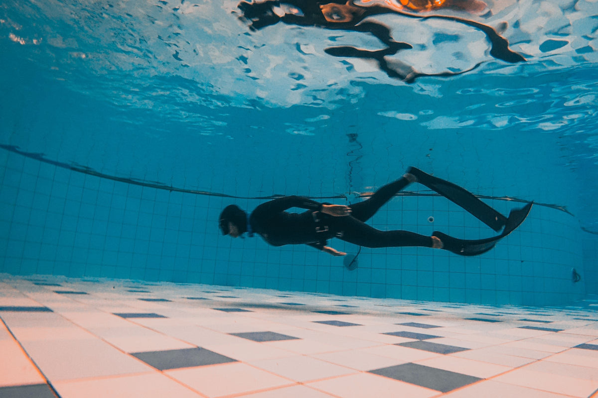 Diver in a wetsuit and fins gliding across the bottom of a tiled indoor training pool