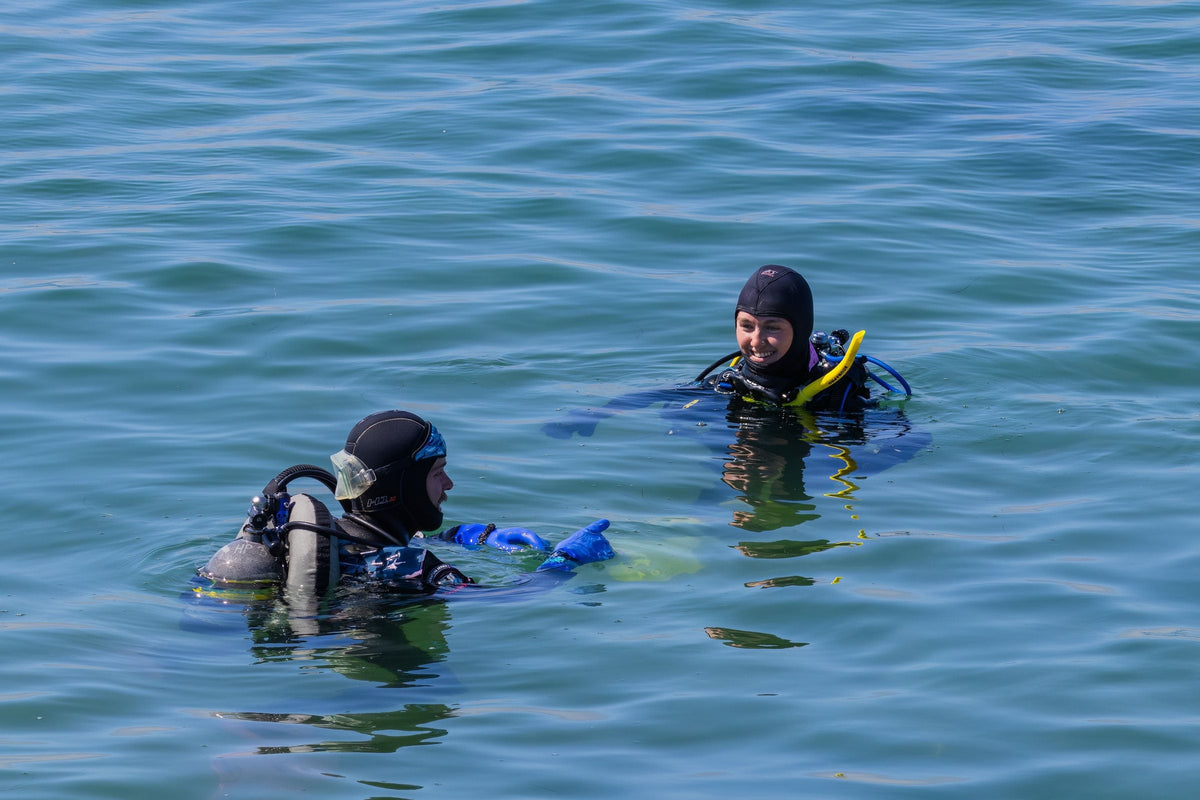 Two divers at the surface in full scuba kit, one coaching the other