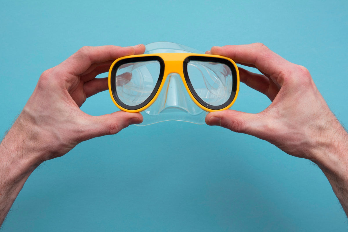A diving mask held in two hands against a flat cyan background.