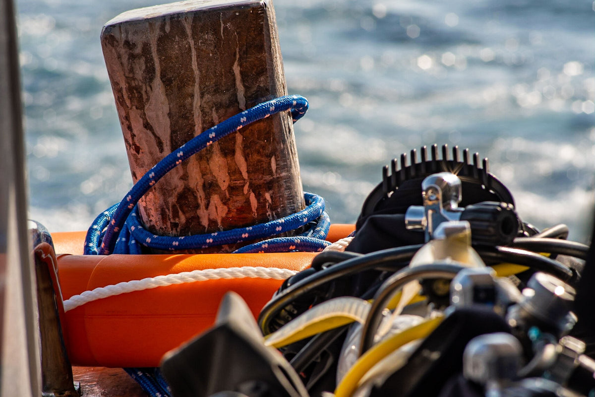 Scuba regulators and buoyancy jackets rigged and waiting beside a mooring post on a boat, low sun on the water