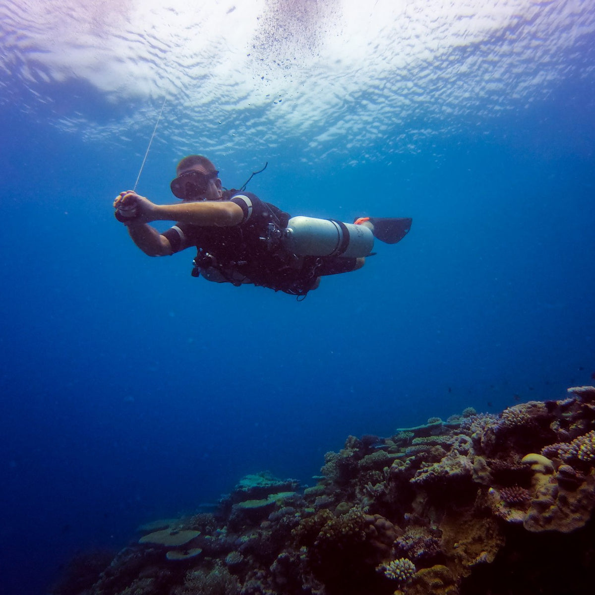 A sidemount diver in trim on a line over a reef