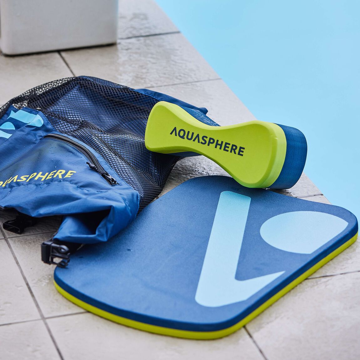 Aquasphere kickboard and pull buoy on a pool deck next to a mesh bag