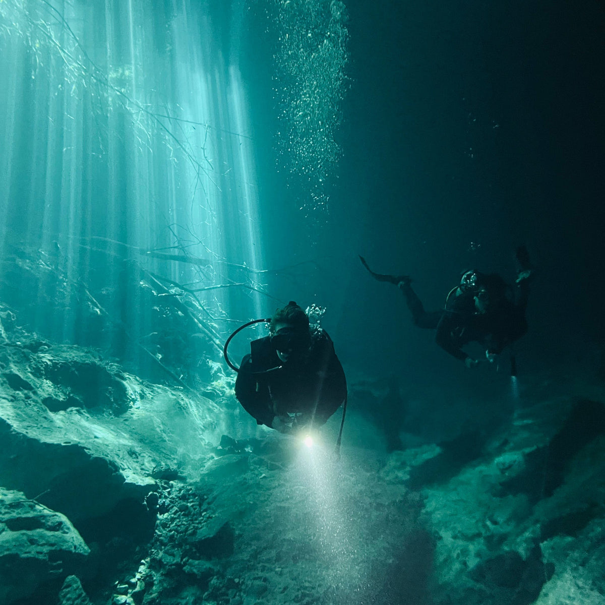 Diver with a torch in a cenote under shafts of daylight in the cavern zone