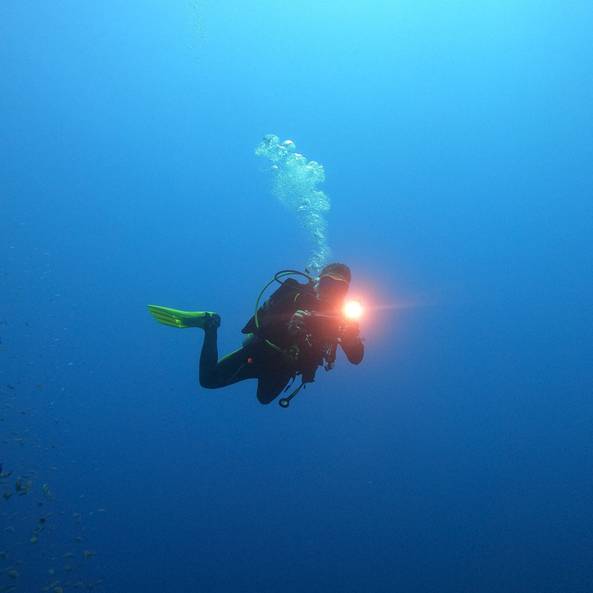 Lone diver with a lit torch in open blue water on a deep dive