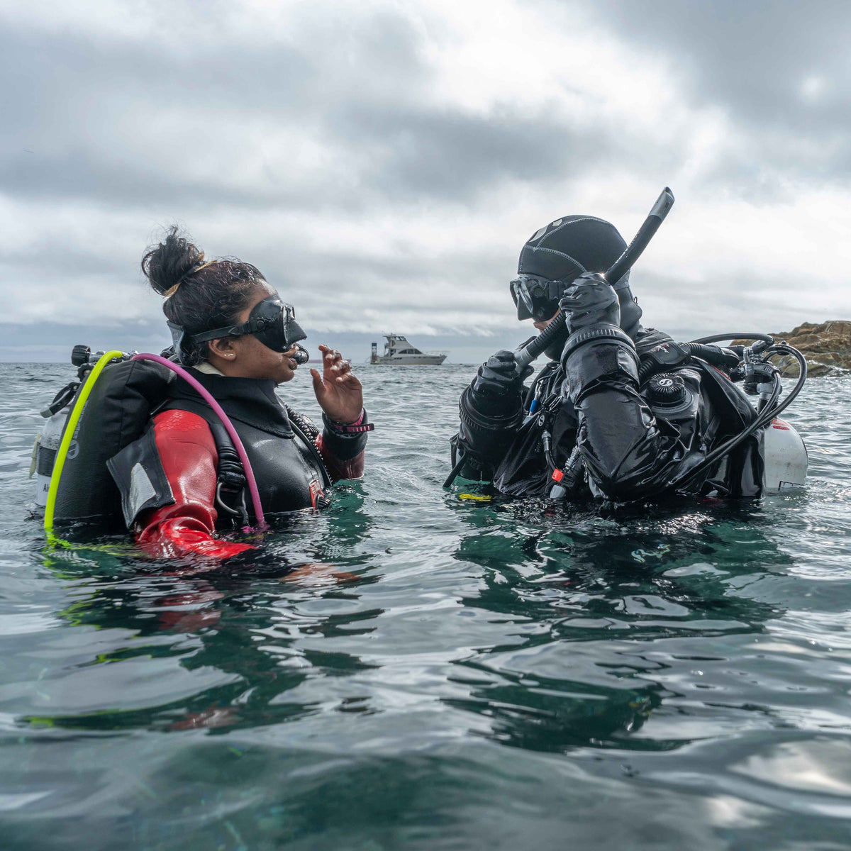 Two drysuit divers at the surface off a rocky shore on a local guided dive