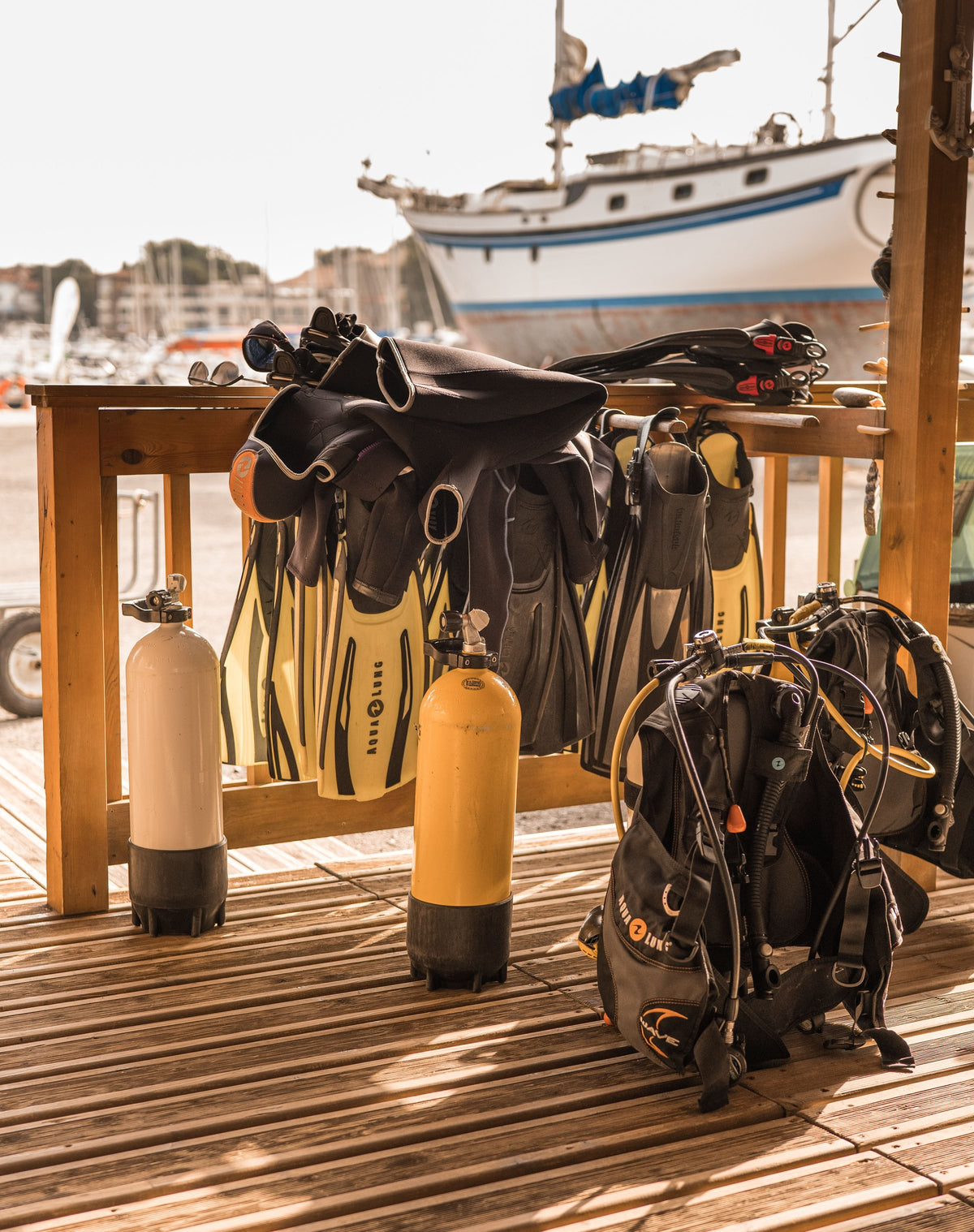 Dive kit laid out on a marina deck with cylinders, fins and BCDs, boat behind