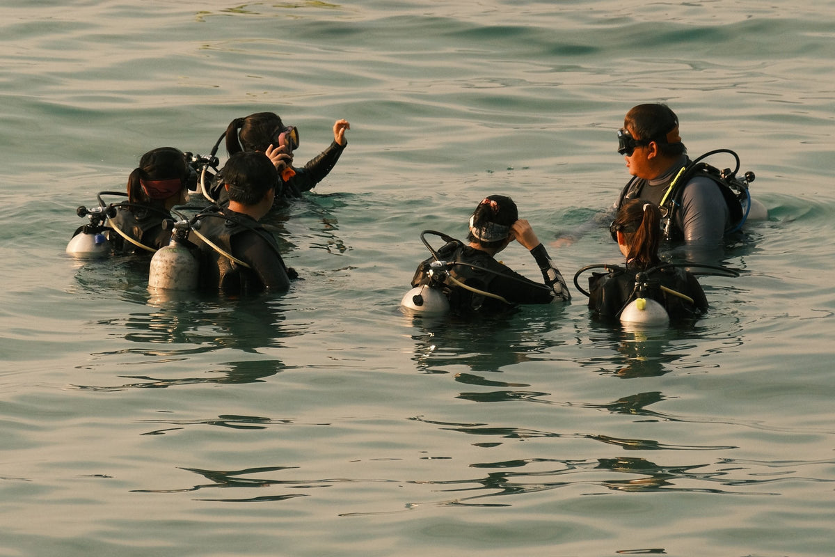 A class of student divers at the surface, kitted up, with the instructor signalling