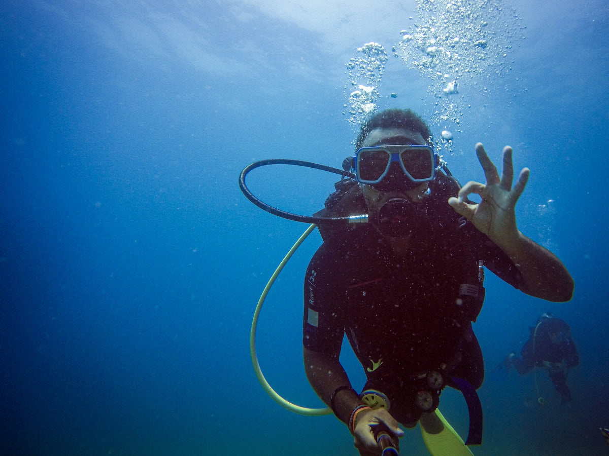 Diver giving a clear OK sign in blue water with bubbles, buddy in the background