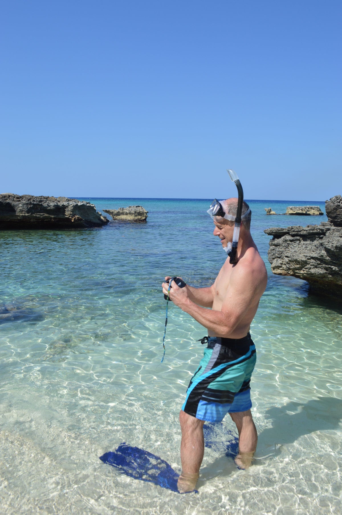 Snorkeller in clear shallows wearing a mask and snorkel, fins in hand