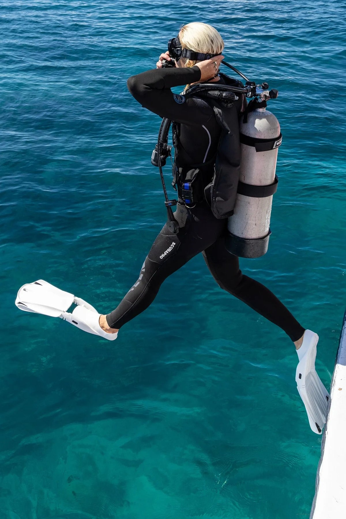 Diver in a full black wetsuit stepping off a dive boat into clear blue water