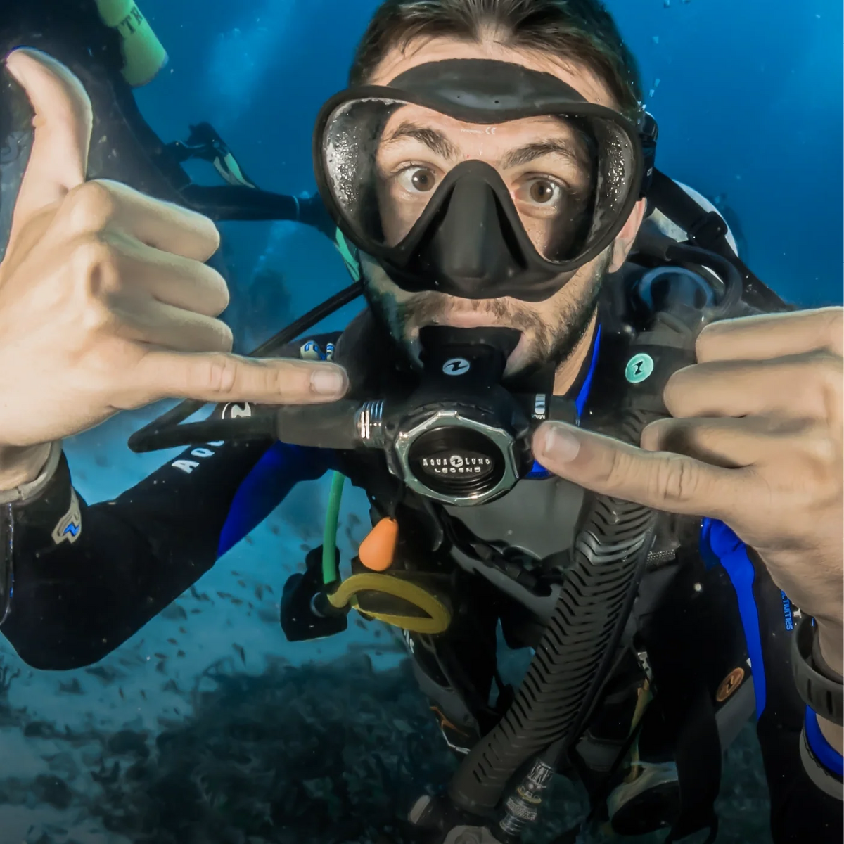 Scuba diver in full kit giving a shaka underwater