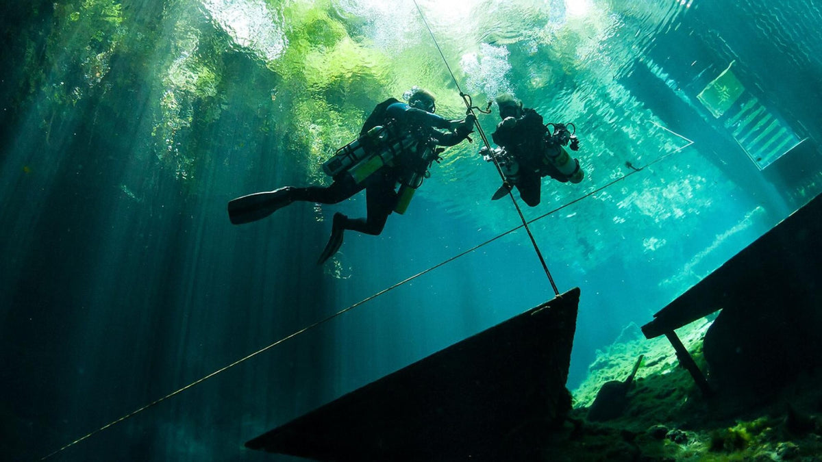 Two sidemount divers on a shot line beneath a boat in clear water