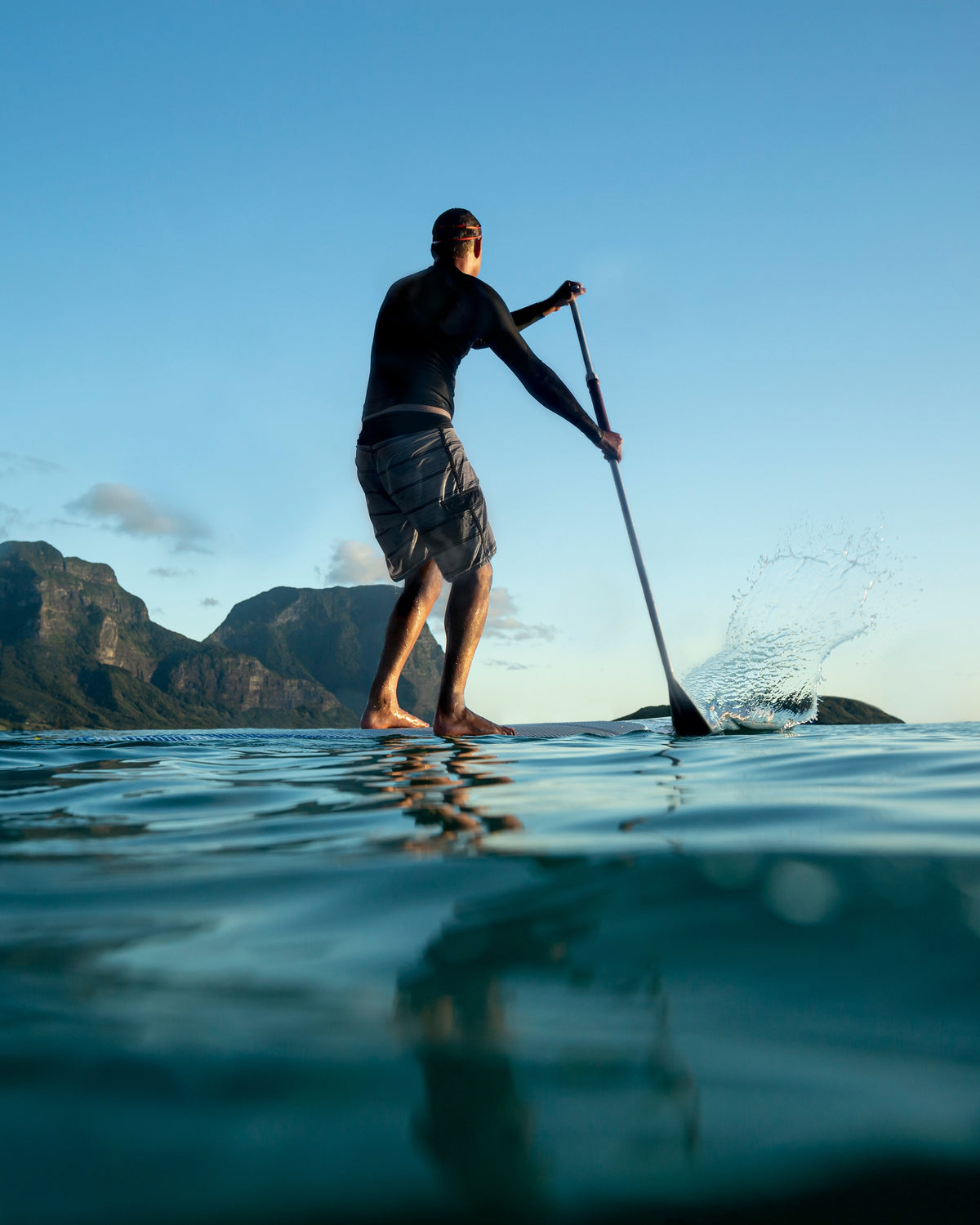 Stand-up paddleboarder on calm water in front of mountains