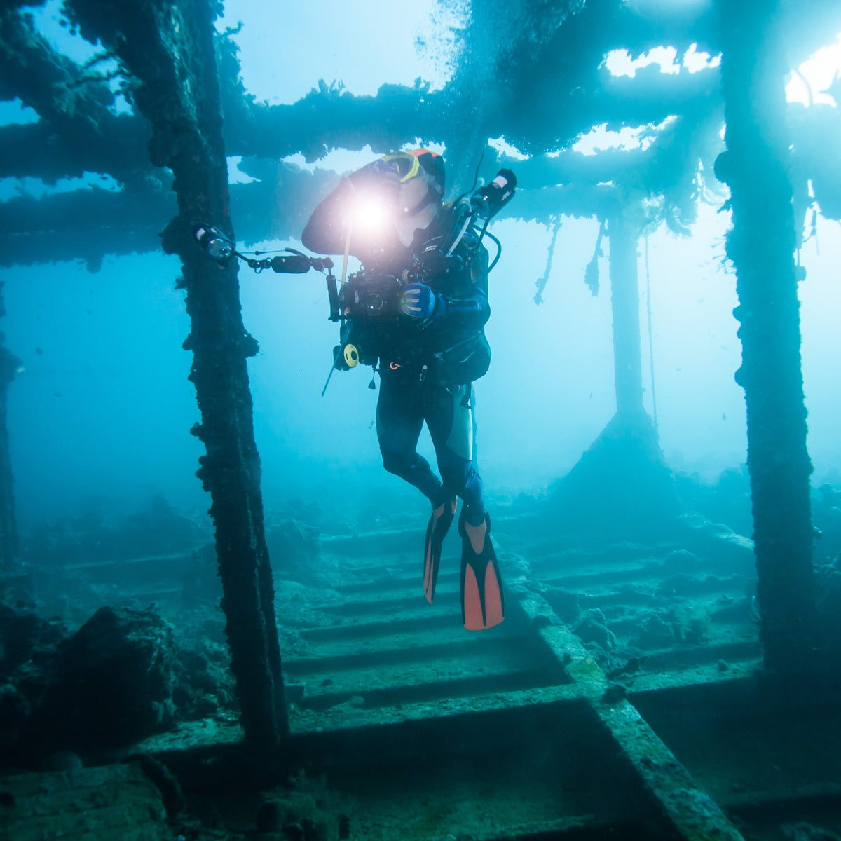Diver with a torch swimming through the open frames of a wreck