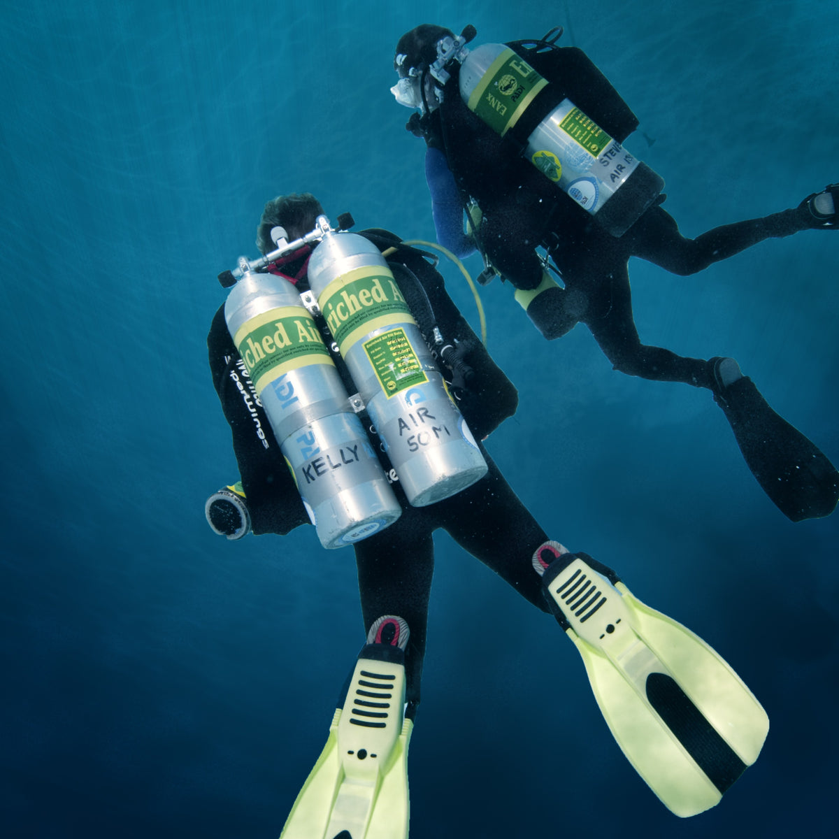Two technical divers in open blue, one in backmounted twins and one carrying a stage