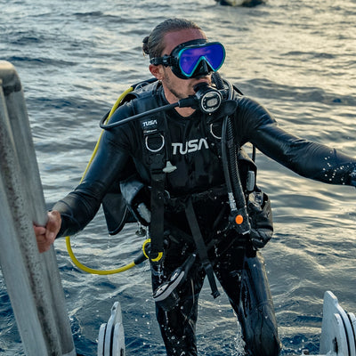 Diver climbing a boat ladder wearing a Tusa BB React BCD