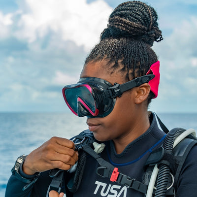 Diver on a boat adjusting a black and pink Tusa Ino mask