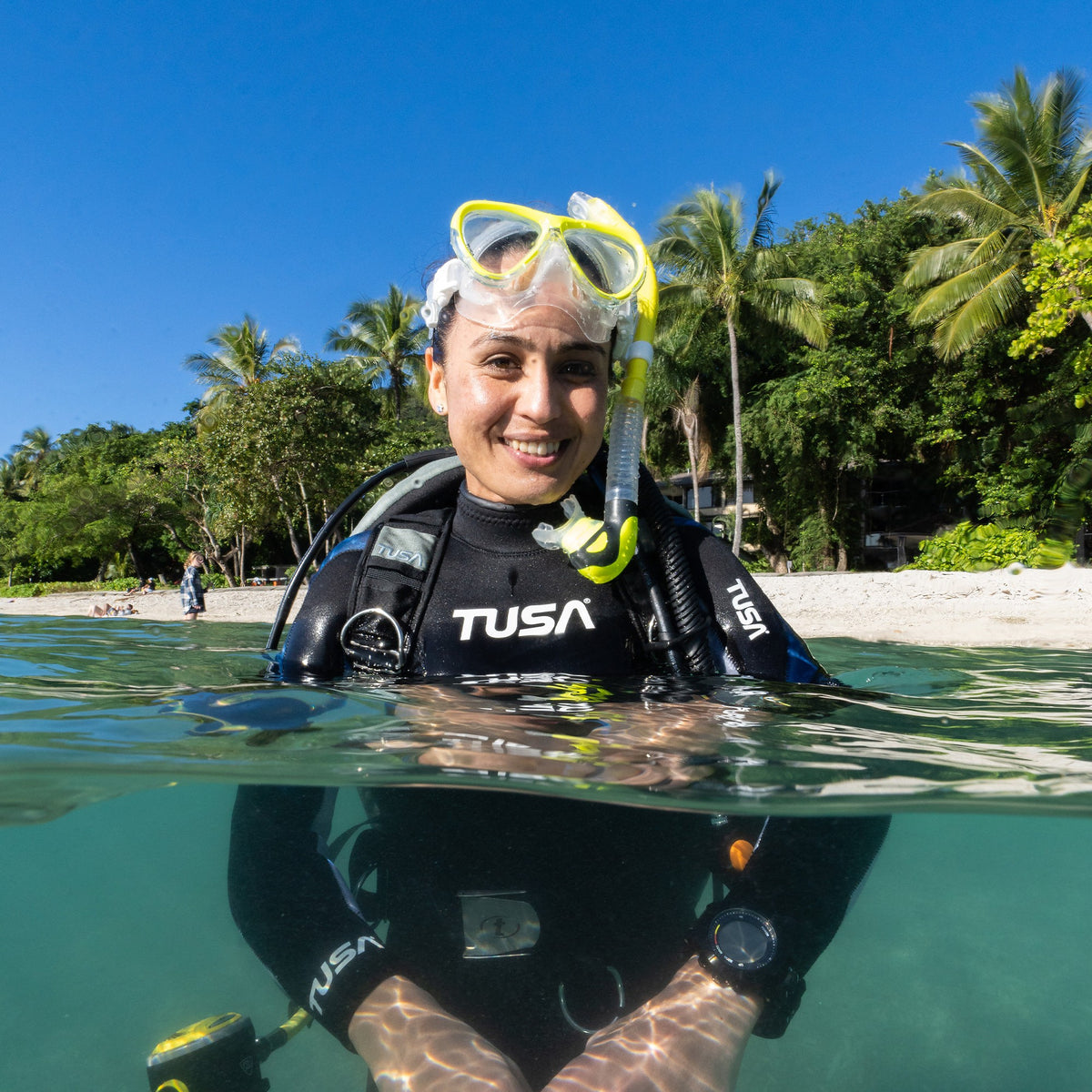 Diver in shallow water on a tropical beach wearing a Tusa Intega mask