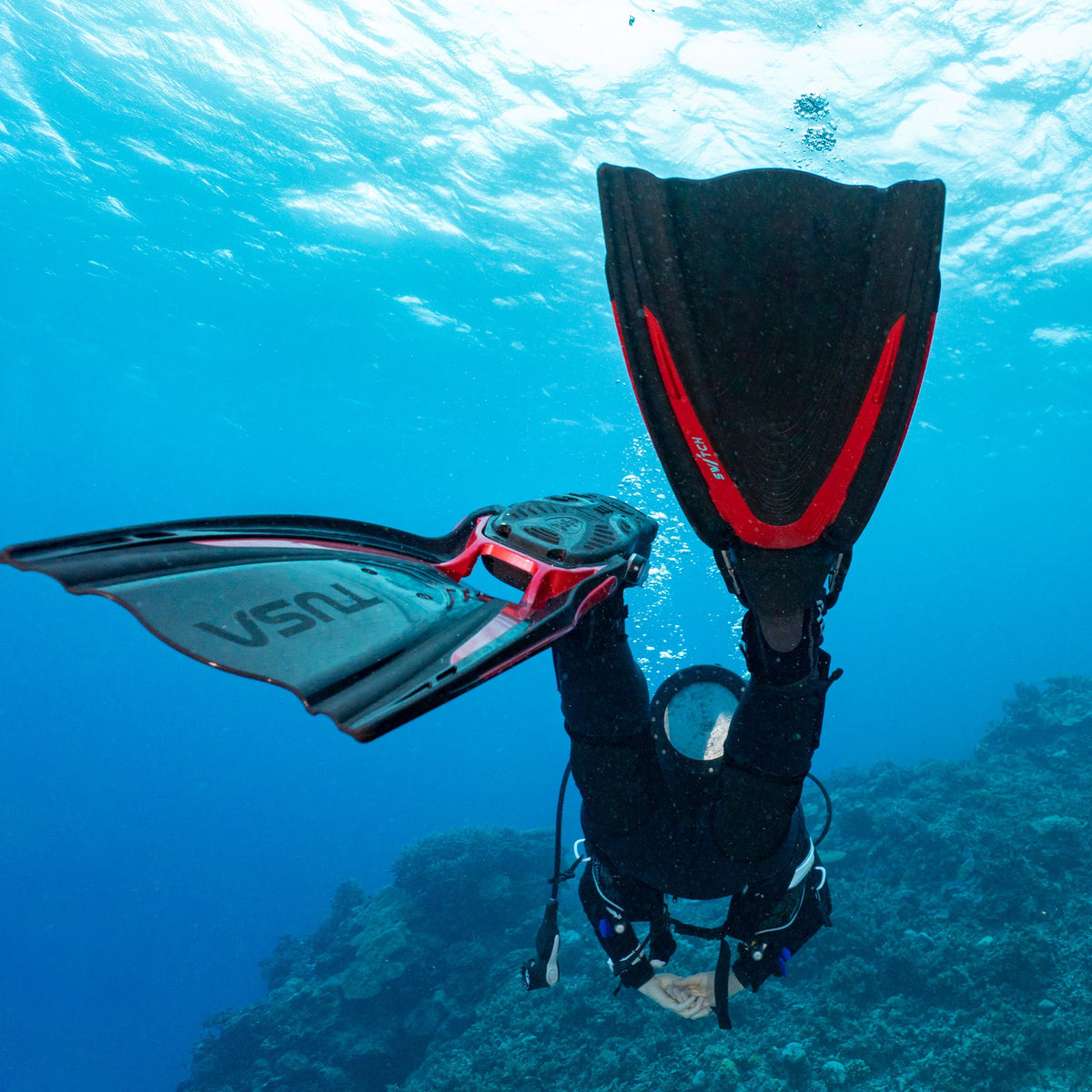 Diver kicking with red Tusa Hyflex Switch fins over a reef