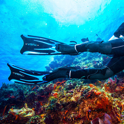 Two divers finning over a reef wearing Tusa Hyflex Vesna fins
